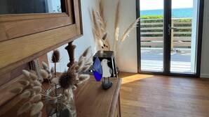 A room with a wooden dresser, a clock on the wall, and a view of the sea through a sliding door.