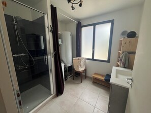 A bathroom with a glass shower enclosure, a white toilet, a wooden bench, and a window with blinds. - Maison de pêcheur vue mer, magnifique en toutes saisons ! (Clohars-Carnoët)