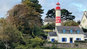 A coastal building with a lighthouse, boats, and a rocky shoreline.