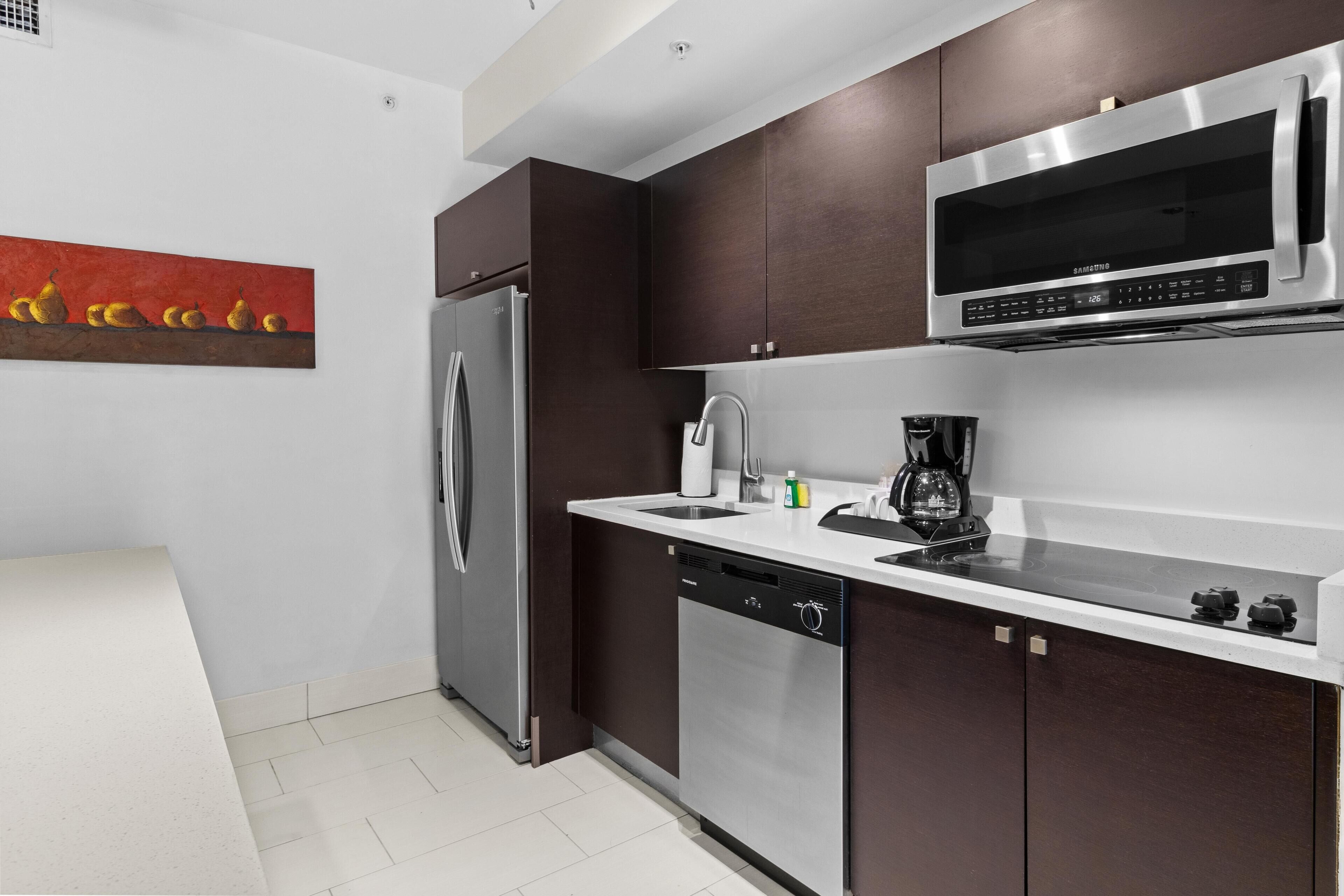 A modern kitchen with dark cabinets, stainless steel appliances, and a white countertop.