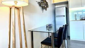 A modern kitchen with a glass-top dining table, black chairs, a refrigerator, and a decorative wall piece. - The Padbury Suites-Premium City Apartment (Bulgarra)