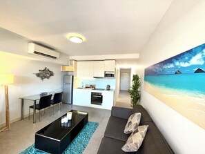 Una sala moderna con una mesa de centro negra, un sofá gris y un cuadro de una playa.