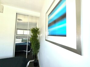 Une chambre à coucher avec un lit, un miroir, une plante en pot et un tableau accroché au mur.