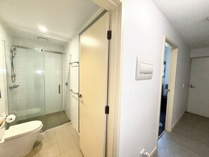 Une salle de bain équipée de toilettes, d’une douche et d’un espace de douche clos par des parois en verre.