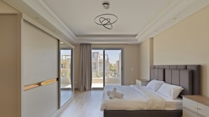 A modern hotel room with a large bed, a bedside table, a wardrobe, and a balcony with a view of the city. - ALSAWAH Spacious Family Villa in Palm Hills Sheikh Zayed (6th of October City)