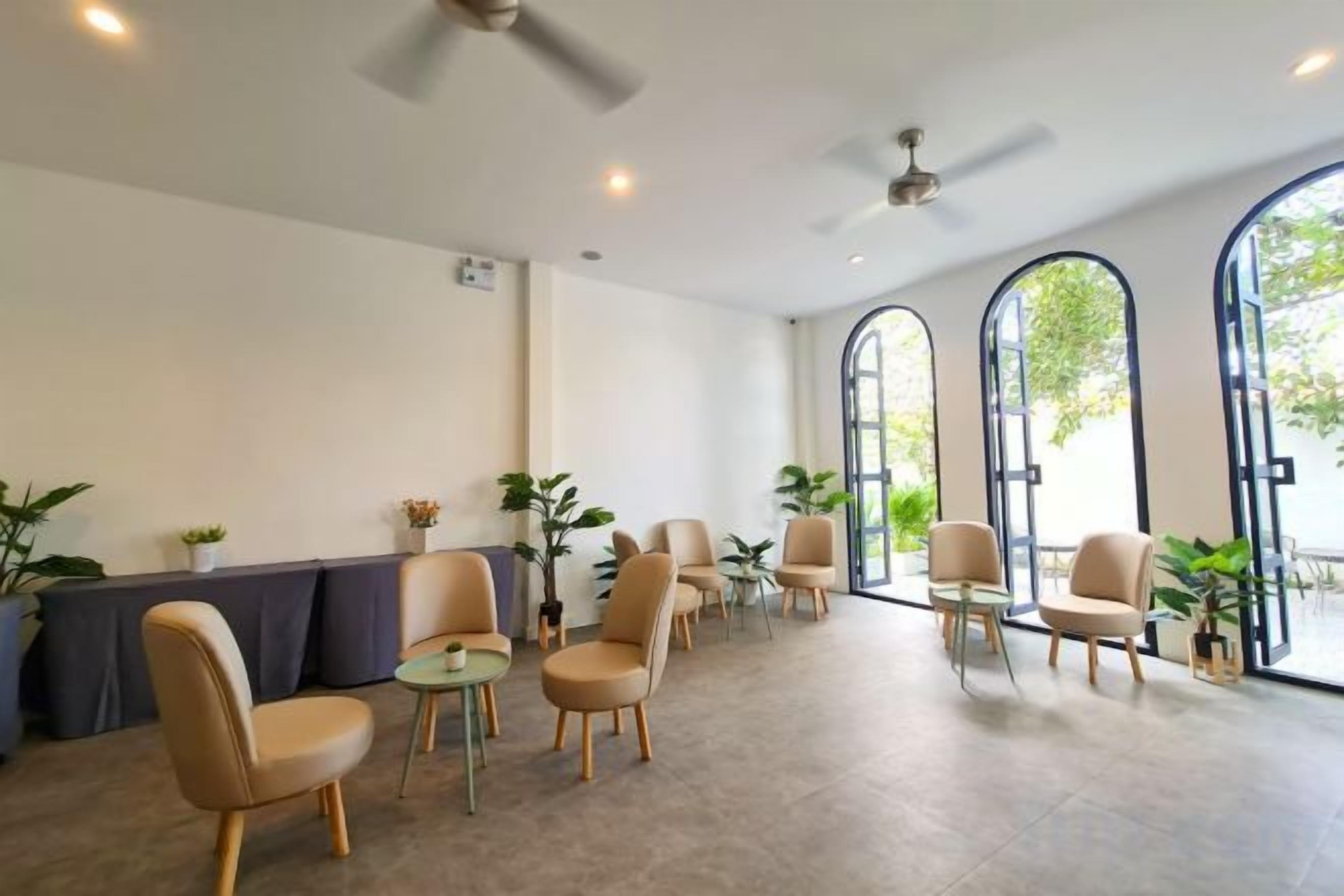 A spacious indoor area with multiple seating arrangements, including chairs and tables, and large windows allowing natural light.
