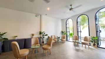 A spacious indoor area with multiple seating arrangements, including chairs and tables, and large windows allowing natural light.