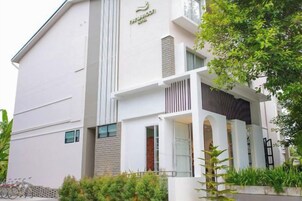A modern hotel with a white facade, a balcony with a railing, and a sign indicating it is a hotel.