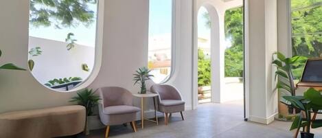 A spacious room with a curved window, a small table, two chairs, a bench, and potted plants.