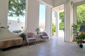 Une pièce spacieuse avec une grande fenêtre, un miroir rond, un banc, deux chaises et une petite table.