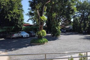 Ein Parkplatz mit mehreren Autos, einem großen Baum und einem Gebäude mit rotem Dach im Hintergrund.