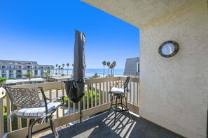 A balcony with a view of the beach, a clock, and two chairs. - Coastal Luxury! Oceanview 1-Bedroom Retreat at North Coast Village C312 (Oceanside)
