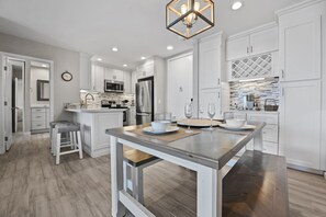 A modern kitchen with white cabinetry, a central island, and a dining area with a wooden table.