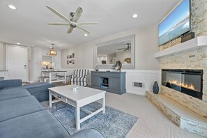 Ein modernes Wohnzimmer mit Kamin, Deckenventilator und Meerblick durch ein großes Fenster.