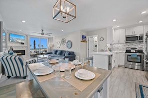 A modern living room with a fireplace, a dining area set for four, and a kitchen with stainless steel appliances. - Coastal Luxury! Oceanview 1-Bedroom Retreat at North Coast Village C312 (Oceanside)