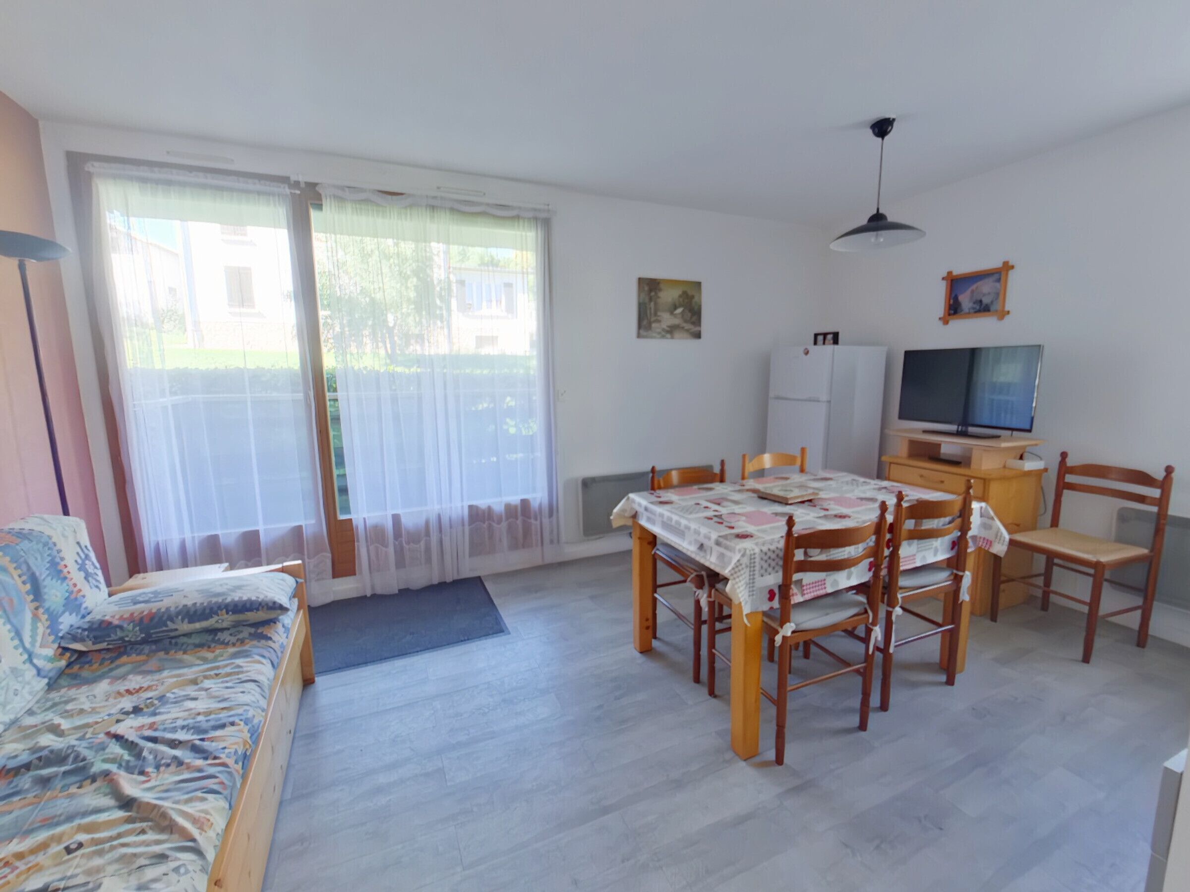Ein Zimmer mit einer Couch, einem Esstisch mit Stühlen, einem Fernseher und einem Kühlschrank.