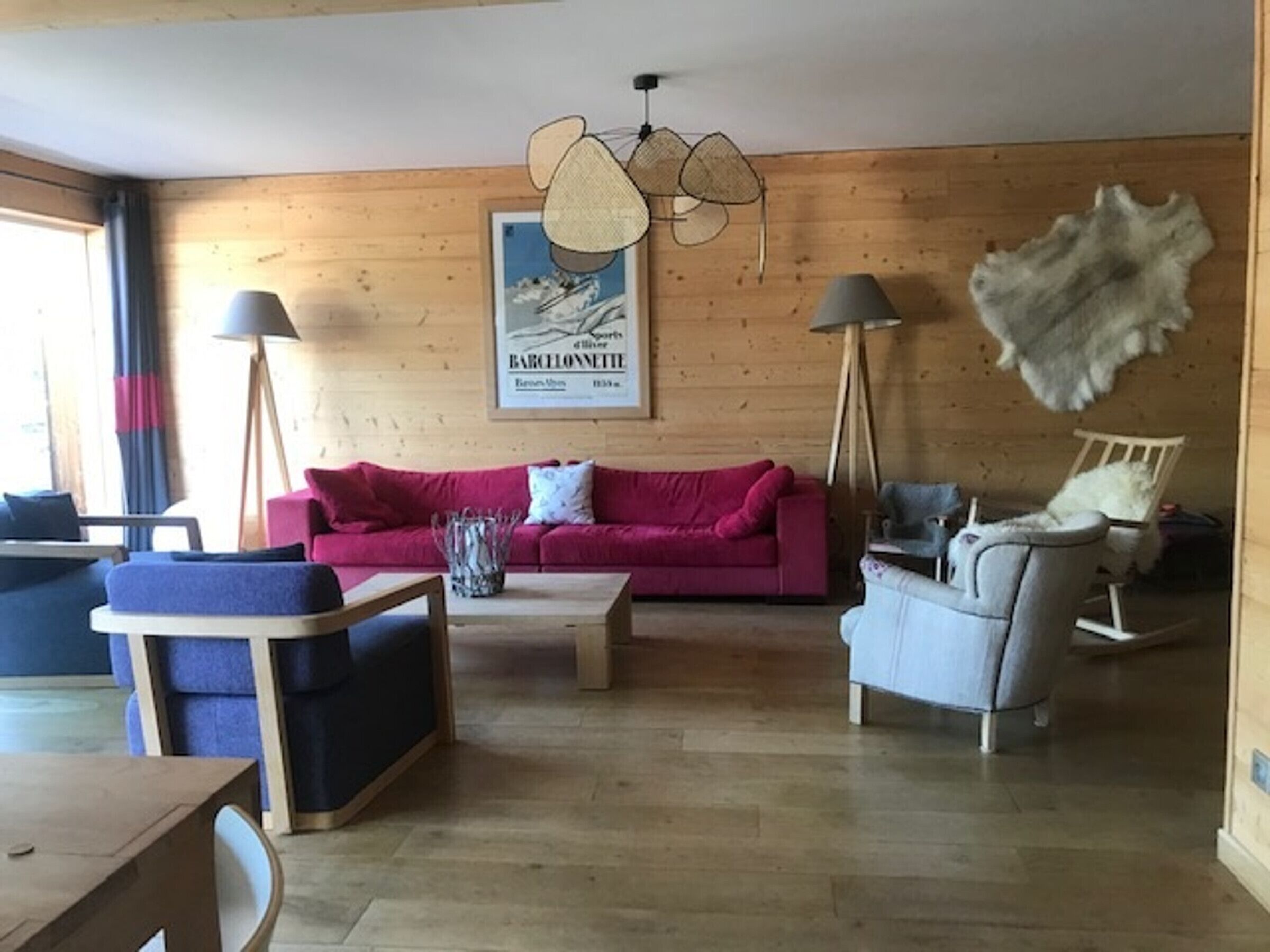 Un salón acogedor con una pared de madera, un sofá rojo, un sillón azul y un sillón blanco, junto con una mesa de centro.