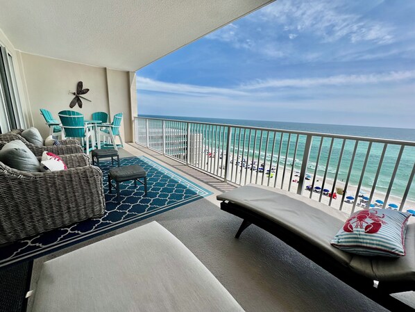 A balcony with wicker furniture, a view of the beach, and a railing.