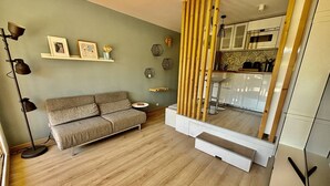 A living room with a sofa, a coffee table, a floor lamp, and a kitchen area with cabinets and a microwave.