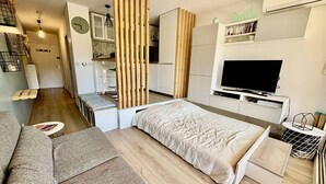 A modern, compact bedroom with a bed, a small desk, a TV, and a bookshelf.
