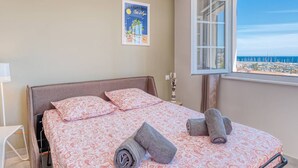 A bedroom with a bed, pillows, a window with a view, and a poster on the wall. - Air-Conditioned Apartment in Le Lavandou Center, Near Beach (Le Lavandou)