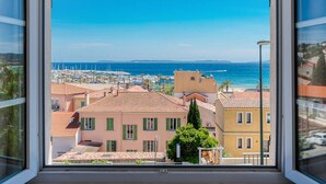 A window view of a coastal town with buildings, a marina, and the sea. - Air-Conditioned Apartment in Le Lavandou Center, Near Beach (Le Lavandou)
