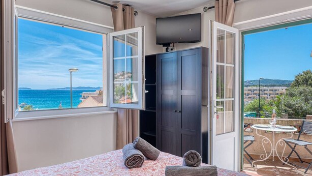 A bedroom with a bed, a TV, a wardrobe, and a balcony with a table and chairs. - Air-Conditioned Apartment in Le Lavandou Center, Near Beach (Le Lavandou)