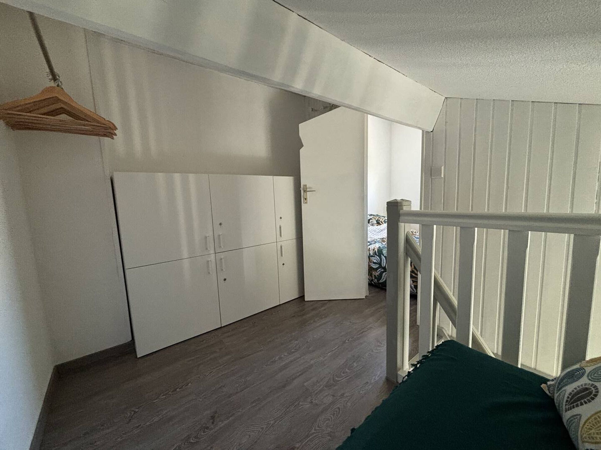 A room with a wardrobe, a bed with a green pillow, and a wooden floor.