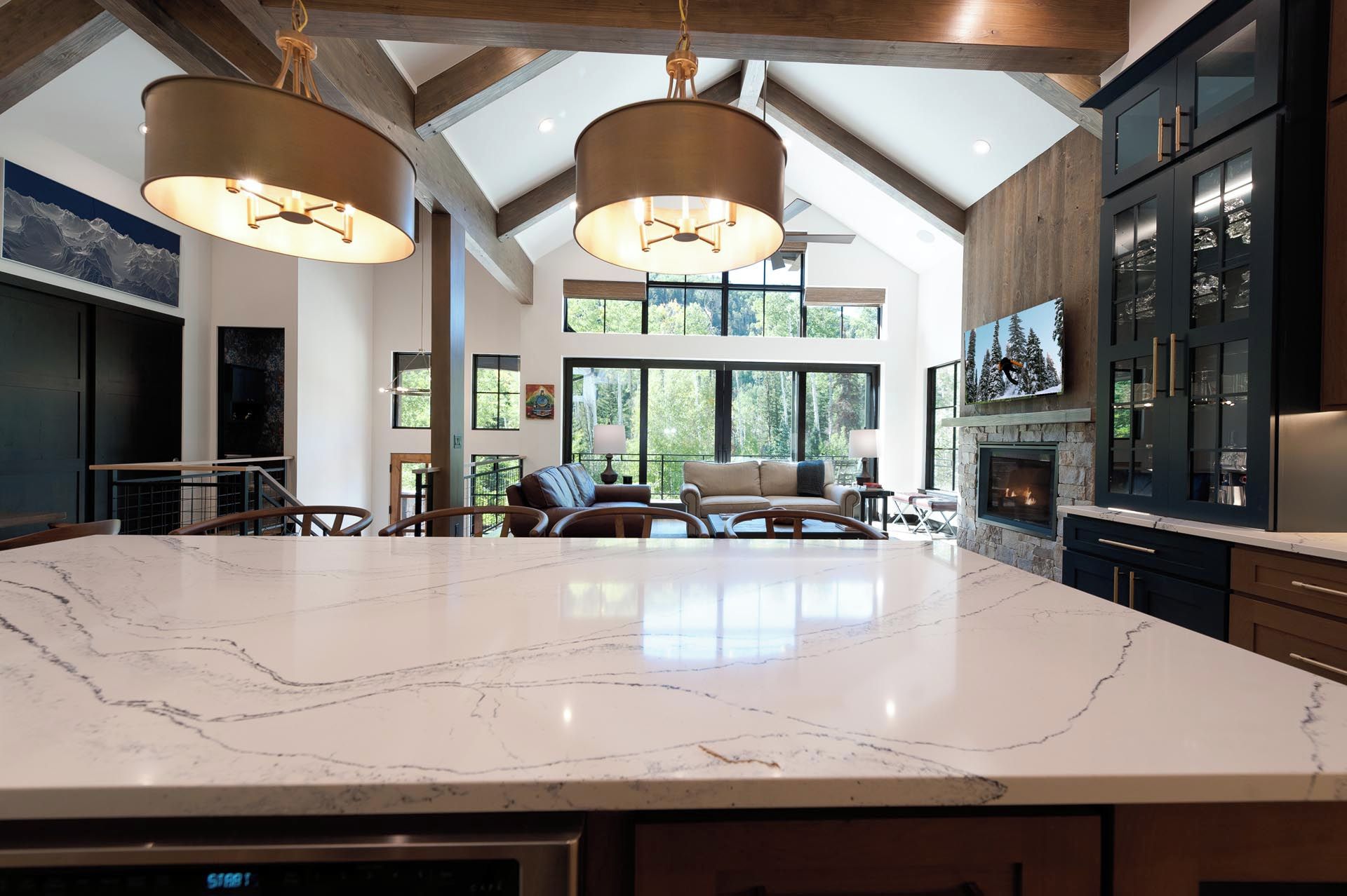 A spacious kitchen with a large marble island, wooden beams, and a stone fireplace.