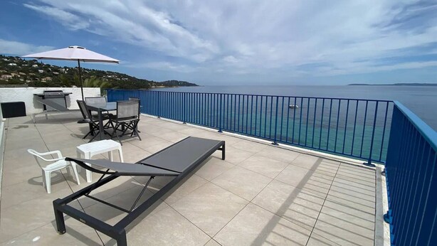 Une terrasse avec une table, des chaises, un transat et un barbecue.