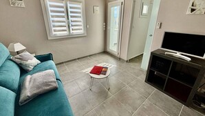 Un salon avec un canapé de couleur turquoise, une petite table sur laquelle repose un livre, un téléviseur posé sur un meuble et une porte-fenêtre coulissante donnant sur un balcon.
