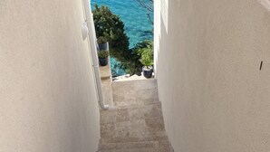 Un escalier en béton menant à un balcon agrémenté de plantes en pot et offrant une vue sur la mer.