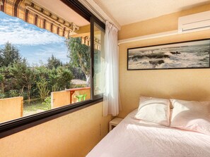 Una habitación de hotel con cama, ventana con vistas a árboles y un balcón, además de un cuadro en la pared.
