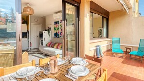 Un coin repas avec une table en bois dressée pour quatre personnes, un canapé agrémenté de coussins colorés et une vue sur l’intérieur à travers une porte vitrée.