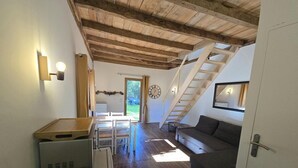 A compact living space with a wooden ceiling, a sofa, a dining table, and a staircase leading to an outdoor area.