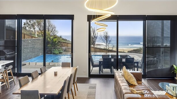 Un salon moderne avec un coin repas, de grandes portes vitrées et une vue sur l’océan.