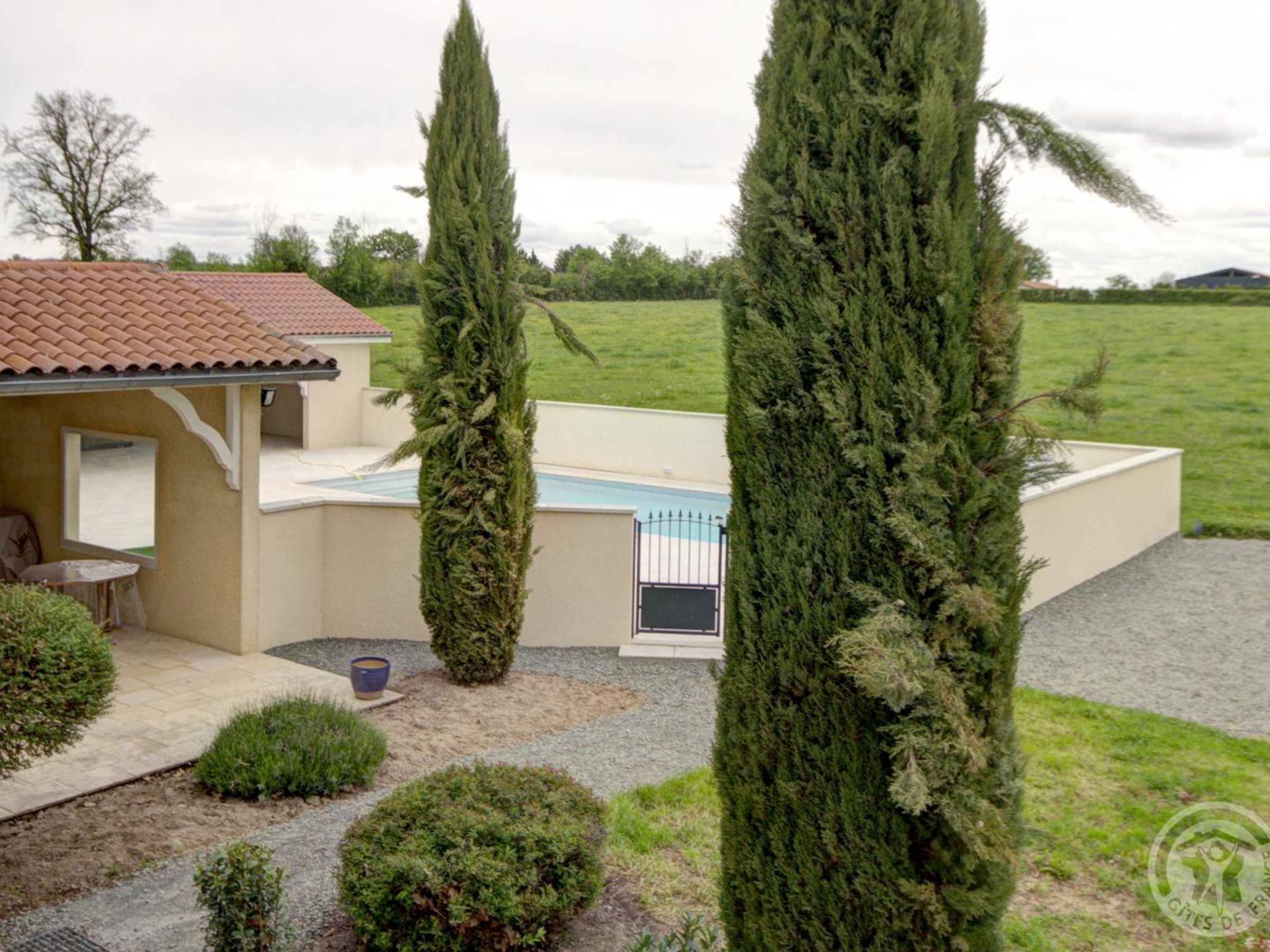 A house with a swimming pool, surrounded by well-maintained hedges and tall trees.