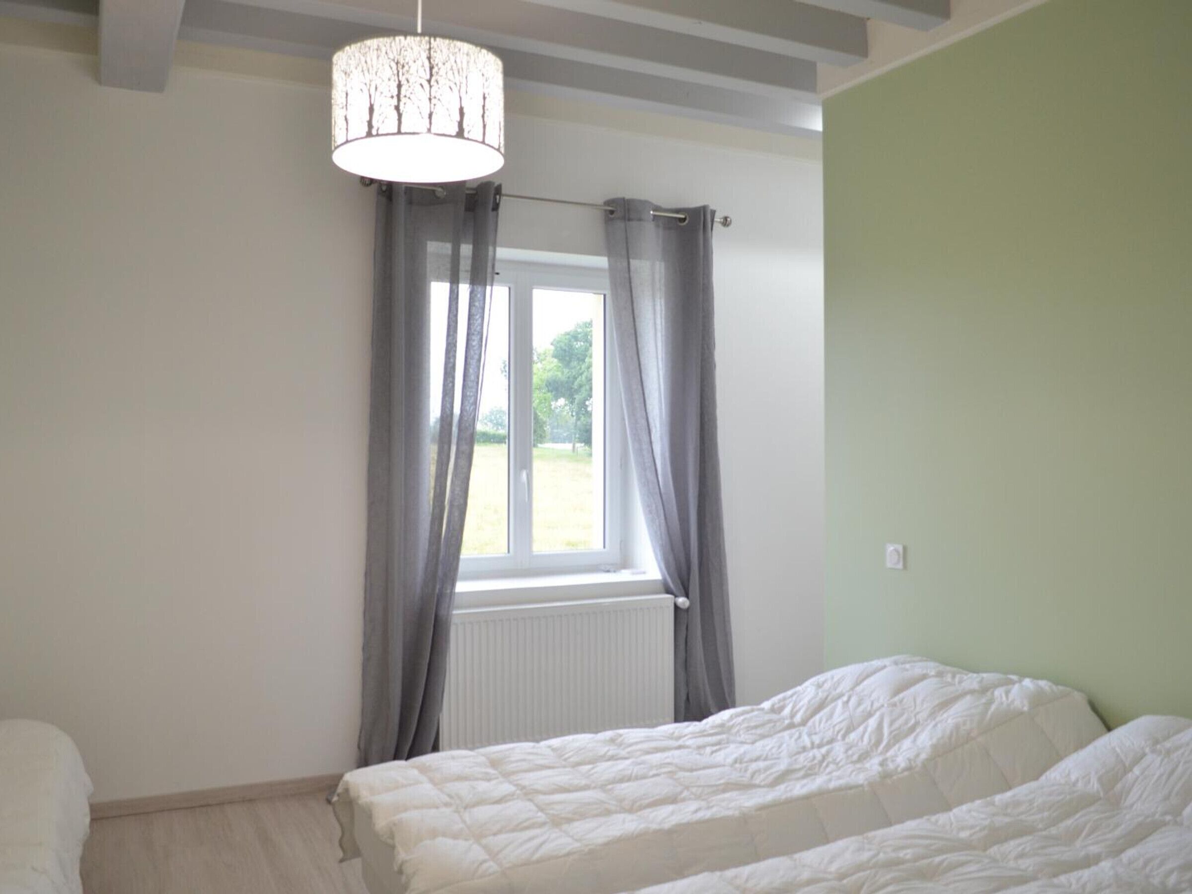 Ein Schlafzimmer mit Bett, einem Fenster mit Vorhängen, einem Heizkörper und einer Pendelleuchte.