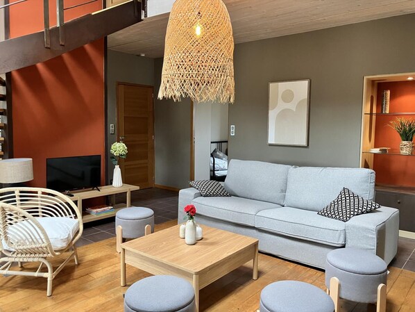 A modern living room with a grey sofa, wooden coffee table, wicker chair, and a hanging light fixture.