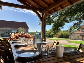 An outdoor dining area with a wooden table set for a meal, surrounded by chairs, and a pergola overhead.