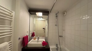 Een badkamer met een witte wastafel, een spiegel, een douche en een handdoekhouder.
