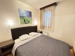 A bedroom with a large bed, a headboard, two bedside tables, a wall-mounted lamp, and a window with curtains. - Bright 3-room apartment near slopes with balcony and parking (Serre Chevalier Chantemerle)
