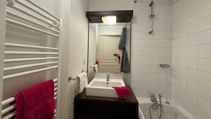 Een badkamer met een witte badkuip, een wastafel met spiegel erboven en een handdoekhouder met een rode handdoek.