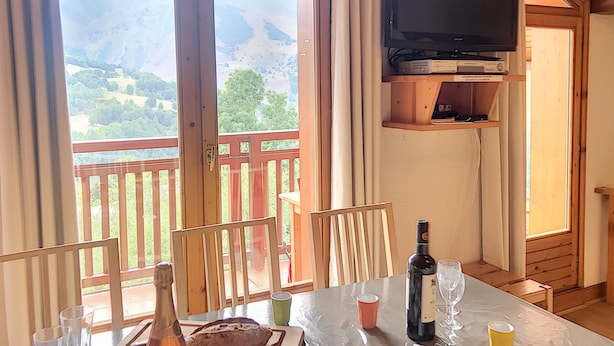 Una zona de menjador amb una taula preparada per a dues persones, una ampolla de vi i un televisor penjat sobre la taula.