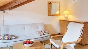 Una habitació acollidora amb un sofà blanc, una cadira de fusta, una taula petita amb un bol de fruita, un mirall i una làmpada.