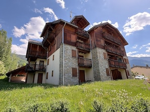 A multi-story wooden building with balconies, stone pillars, and a mountainous backdrop.