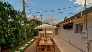 Un patio con una mesa y sillas de madera, una parrilla y un televisor montado en la pared.