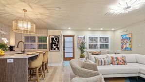 Una cocina moderna con una isla central, taburetes de bar y un comedor con sofá blanco y cojines coloridos.