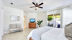 A bedroom with a bed, a TV, a sofa, a wooden dresser, and a ceiling fan. - Dolphin Dreams | Private Pool | Naples Park Retreat (Naples)