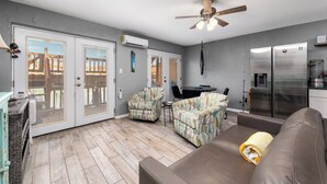 A living room with a sofa, two armchairs, a ceiling fan, and a kitchen area with a refrigerator.
